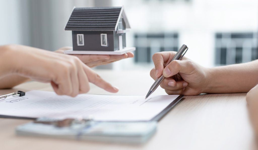 person holding a house tells another to sign an agreement
